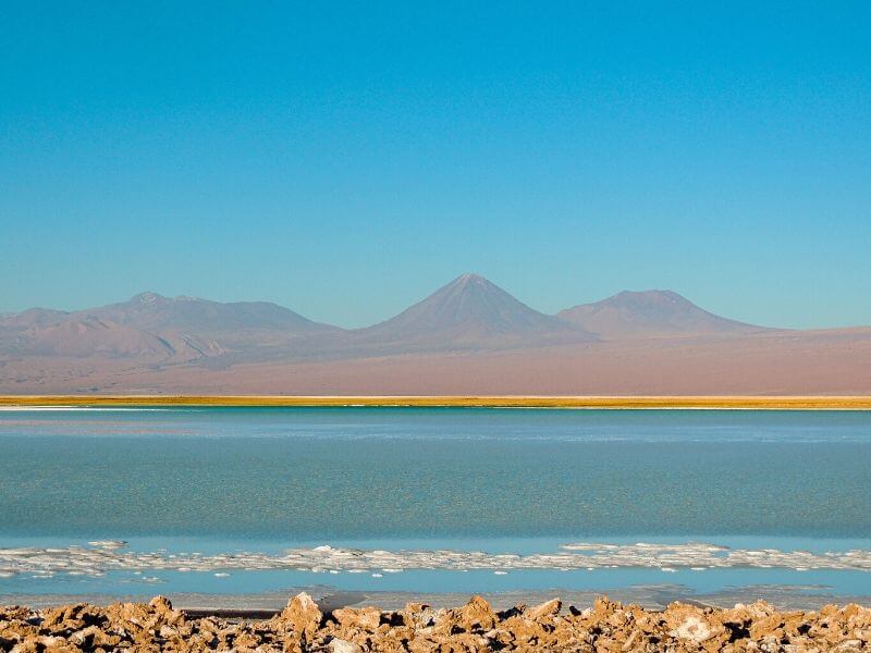 Contraste do Deserto entre o azul da água do salar, o verde da vegetação e o vermelho dos vulcões