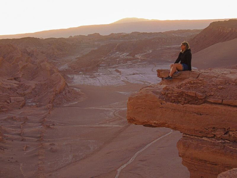 Paisagem do Vale da Lua no Deserto do Atacama ao por do sol, com menina sentada na Pedra do Coyote