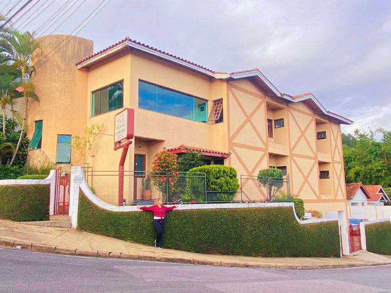 Pousada em tom amarelo com moça de vermelho e preto na frente onde ficar em Atibaia